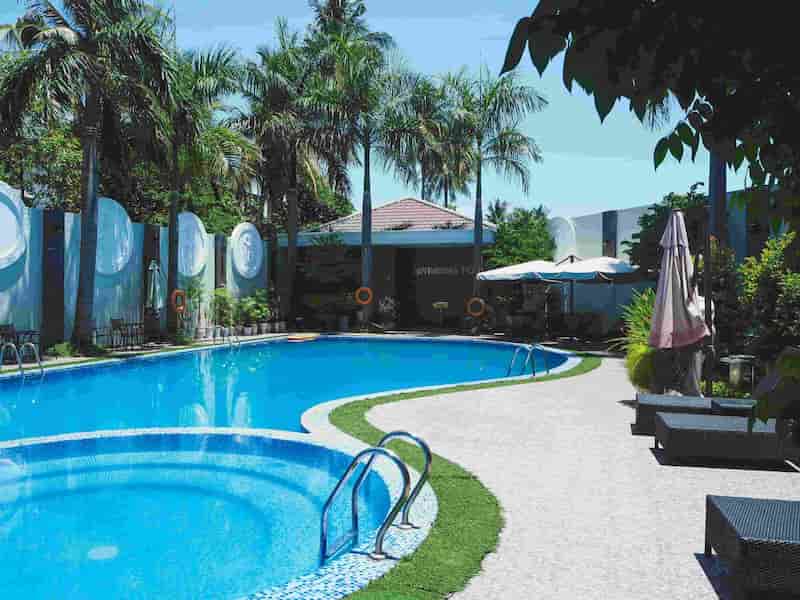Outdoor swimming pool with palm trees, sun loungers and umbrellas in a tropical resort setting